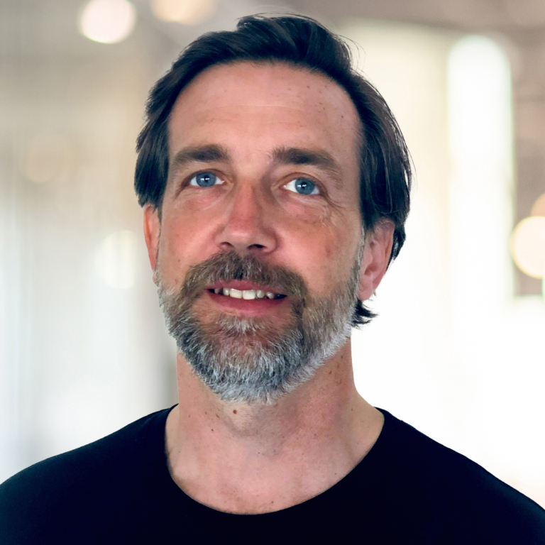 A blue-eyed man with short, dark hair and a neatly-trimmed, greying beard.