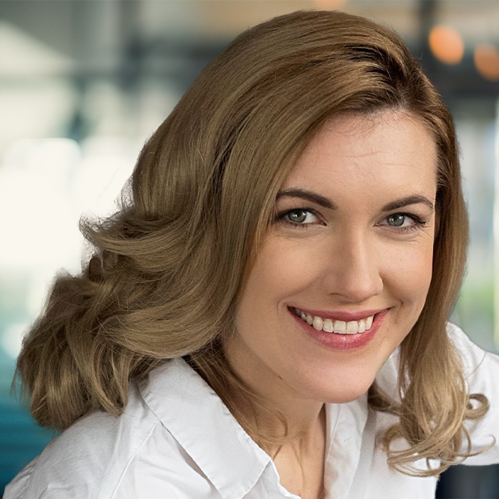 A smiling woman with grey eyes and curly, dark blonde hair.